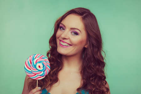 Woman attractive cheerful girl holding colorful lollipop candy in hand. Sweet food and enjoying concept. Studio shot green blue background, toned imageの写真素材