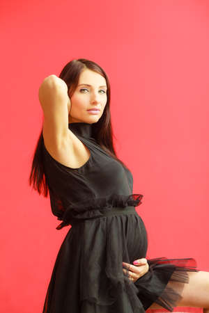 Stylish pretty girl in black evening dress. Pregnant woman preparing for event. Glamour look. Prospective mothering concept.の写真素材