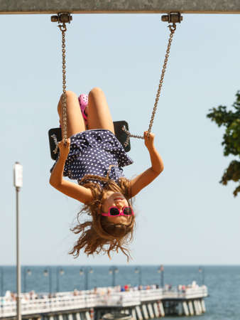 Craziness and freedom. Young summer girl playing on swing-set outdoor. Crazy playful child swinging...