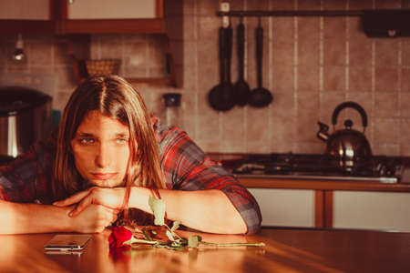 Disappointment and depression. Unrequited love concept. Young worried disappointed man with single red rose and smartphone mobile phone waiting for his girlfriend.の写真素材