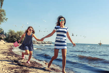 Happy carefree family running on beach at sea coast. Little girl kid with mother having fun. Summer holidays vacation. Happiness.の写真素材