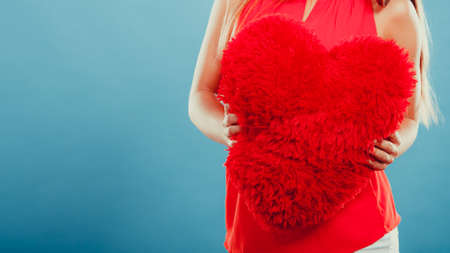 Red heart shape pillow in human hands in studio on blue. Valentines day love.の写真素材