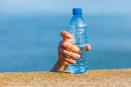 Male hand taking away water plastic bottle outdoor on sea shoreの写真素材