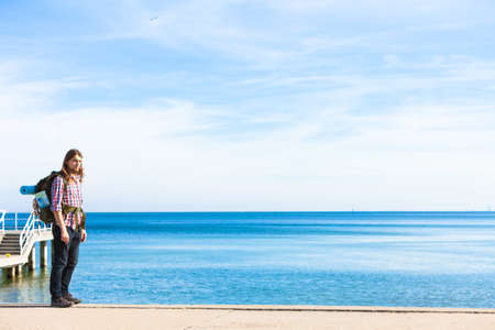 Man hiker backpacker walking with backpack by seaside at sunny day. Adventure, summer, tourism...