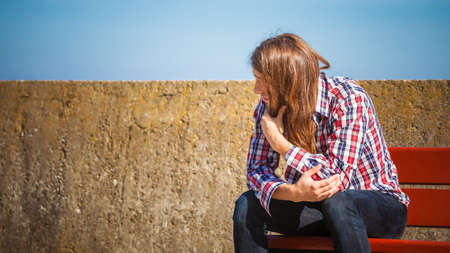 Man bearded long hair wearing plaid shirt casual style relaxing outdoor at summer sunny windy day sitting on benchの写真素材