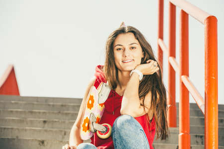 Cool skater young long haired girl with skateboard sitting on the urban stairs. Active lifestyle funky in summer. Outdoor trendy sport teenage.の写真素材