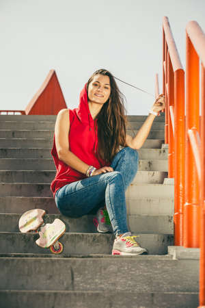 Cool skater young long haired girl with skateboard sitting on the urban stairs. Active lifestyle funky in summer. Outdoor trendy sport teenage.の写真素材