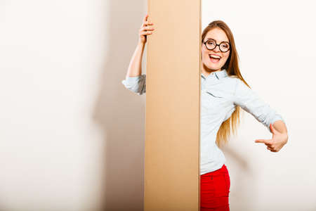 Happy woman moving into new apartment house holding carton box with furniture. Young girl showing...