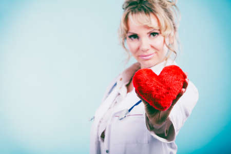 Love from working and helping people. Mid age blonde doctor in white medical apron with heart on blue. Enjoy work concept.の写真素材