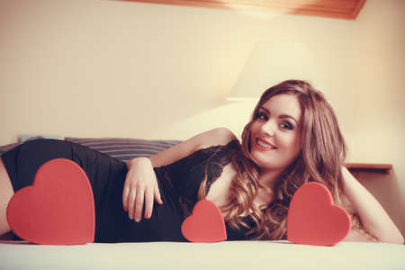 Seductive woman wearing lingerie in bed at home. Attractive sensual young girl with heart shape boxes. Female underwear fashion. Valentines day love.の写真素材