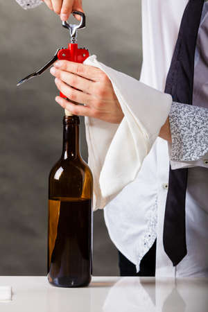 Winery serving tasting alcohol liquor concept. Waiter opens wine bottle. Young male sommelier pulls out cork.の写真素材