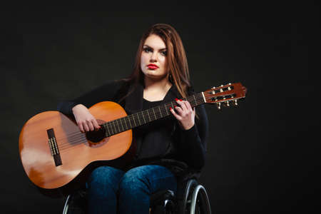 Disabled girl playing guitar. Young female musican on wheelchair. Hobby passion music relax concept.の写真素材