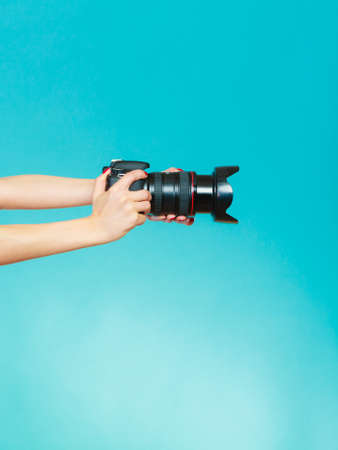 Photographer girl shooting images. woman hands holding camera taking photos. Vivid blue backgroundの写真素材