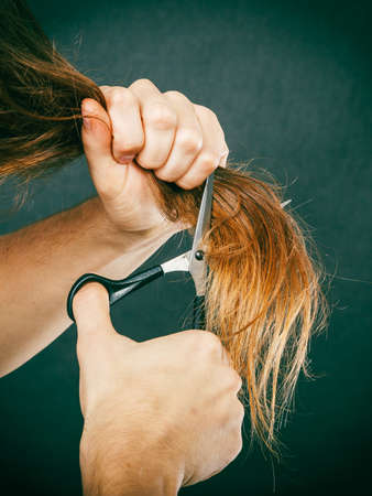 Change of look.  Barber and hairdresser. Male hands with scissors trimmers cutting long brown hair.の写真素材