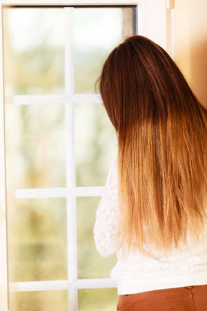 People and solitude concept. alone woman long hair looking dreaming through window back view indoorの写真素材