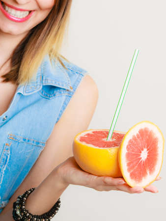 Summer vacation. Happy funny girl tourist holding grapefruit citrus drinking juice from fruit on gray.の写真素材
