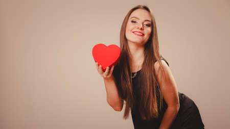 Love help and charity concept. Young beauty happy long haired woman girl in black dress holding heart box gift in studio.の写真素材