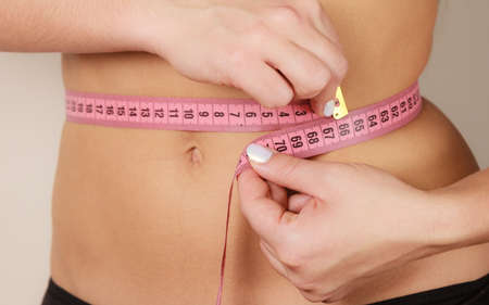Woman fit girl in black lingerie measuring her waist with measure tape closeup. Part of female body.の写真素材