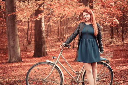 Woodland forest fall outdoor fitness concept. Girl in dress on bike. Young lady in elegant clothes in autumnal park with bicycle.の写真素材