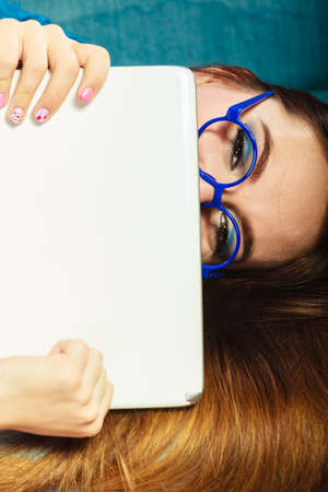 Modern technology education internet concept. Fashion young woman in glasses with tablet relaxing on blue color unusual viewの写真素材