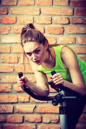 Active young woman working out, doing sport biking in the gym for fitness. Sporty girl training in club. Slim body weight loss concept.の写真素材