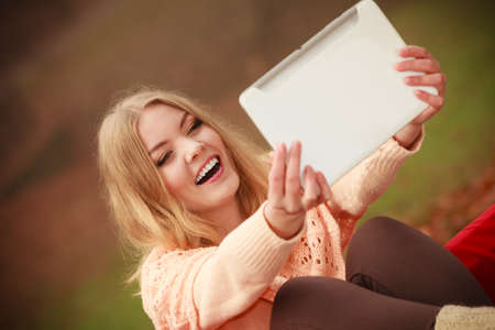 Modern education concept, people outside. Girl sitting on bench with tablet. Attractive young blonde woman with digital equipment.の写真素材