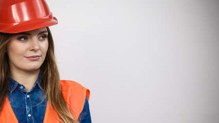 Woman construction worker builder structural engineerin in orange vest red hard helmet. Safety in industrial work. Studio shot on grayの写真素材