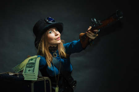 Fashionable subculture weapon concept. Steampunk girl with cash. Young gorgeous lady in victorian fashion lying on floor with banknotes briefcase and blunderbuss.の写真素材