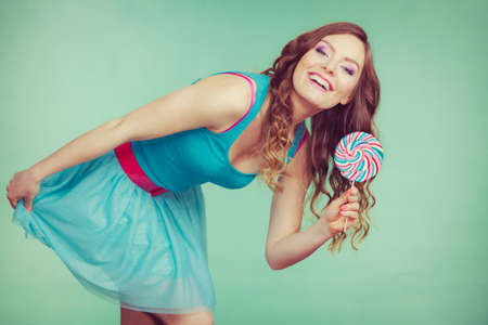 Woman attractive cheerful girl holding colorful lollipop candy in hand. Sweet food and enjoying concept. Studio shot green blue background, toned imageの写真素材