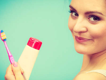 Woman holding brush and tooth paste for teeth cleaning. Happy smiling girl with toothbrush. Oral hygiene. Studio shot green backgroundの写真素材