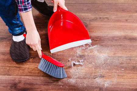 Cleanup housework concept. Closeup cleaning woman sweeping wooden floor with red small whisk broom...