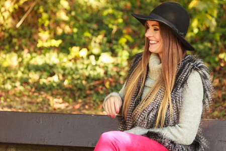 Gorgeous stylish young woman wearing fashionable clothes. Portrait of girl in black hat sitting on bench in park.の写真素材