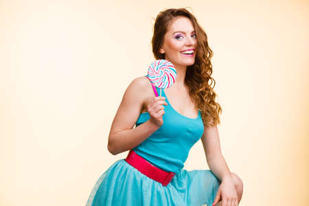 Woman beautiful cheerful girl holding colorful lollipop candy in hand having fun. Sweet food and happiness concept. Studio shot on bright backgroundの写真素材