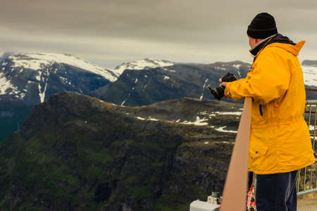 Tourism vacation and travel. Male tourist taking photo with camera, enjoying mountains landscape from Dalsnibba viewpoint, Norway Scandinavia.の写真素材