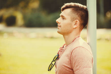 Masculinity handsome outdoor concept. Relaxed boy leaning on pole. Young man chilling in park.の写真素材