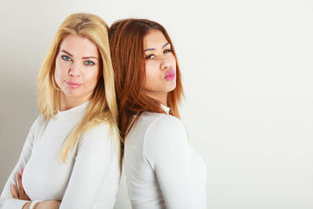 Friends people concept. Two young friends together. Girls have white top, standing next to each other. One lady has blonde hair, second dark ones.の写真素材