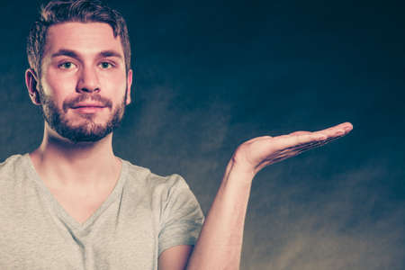 Portrait of handsome man with open empty hand palm for copy space. Young guy in studio on black. Advertisement.の写真素材