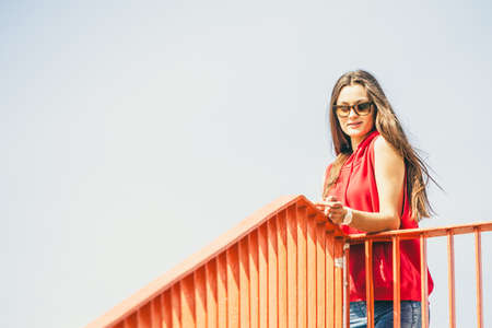 Young long haired girl with sunglasses leaning against railing on the urban bridge. Lifestyle funky...