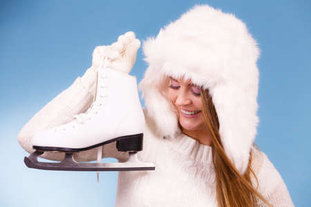 Winter sports clothing concept. Attractive lady with ice skate. Young woman wearing white cozy outfit on blueの写真素材
