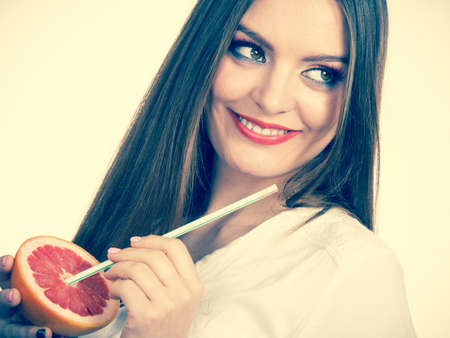 Woman attractive long hair girl eyes makeup holding grapefruit citrus sipping juice from fruit. Healthy diet food. Summer vacation holidays concept. Toned imageの写真素材