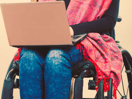 Crippled person with laptop. Young disabled female surfing on web. Internet technology education disability concept.の写真素材