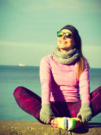 Woman resting relaxing after doing sports outdoors. Fitness girl female jogger wearing warm sporty clothes in cold day weather on seaside taking breakの写真素材