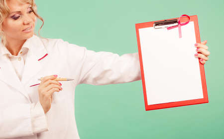 Diagnosis concept. Middle aged female doctor with pen showing red empty folder with pink breast cancer awareness ribbonの写真素材