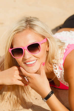 Pretty young blonde pretty girl at beach lying on sand. Woman wearing sunglasses have active time in summer. Summertime and lifestyle concept.の写真素材