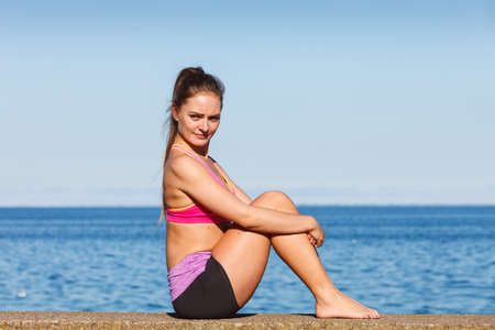Woman doing sports outdoors. Fitness girl in sportswear on seaside exercising keep her body muscles fitの写真素材