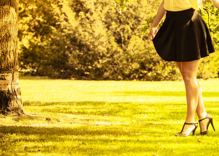 Fashion footwear beauty concept. Female legs in park. Young lady in stilettos and skirt taking walk through park.の写真素材