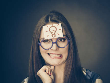 Woman confused thinking seeks a solution, paper card with light idea bulb on her head. Student girl looking for new ideas. Eureka creativity conceptの写真素材