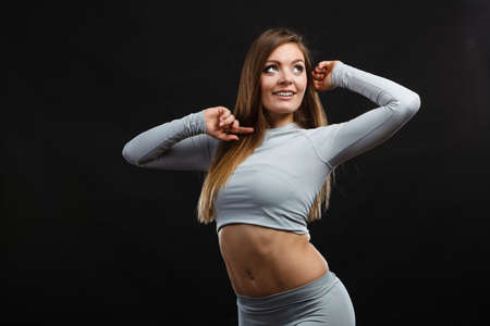 Sporty fitness shape garments concept. Attractive lady in thermal clothes. Young seductive girl pulling shirt showing skin presenting thermoactive clothing on blackの写真素材