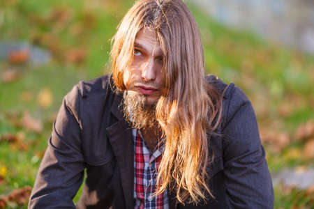 Man long hair sad thoughtful sitting on bench outdoor in autumnal park