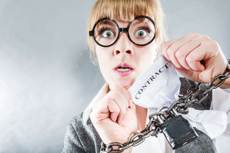 Business and stress concept. Furious businesswoman in glasses with chained hands holding contract grunge background unusual angle viewの写真素材